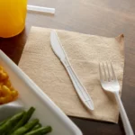 Disposable plastic cutlery on beige napkin, clean restaurant table setting for hygienic dining.