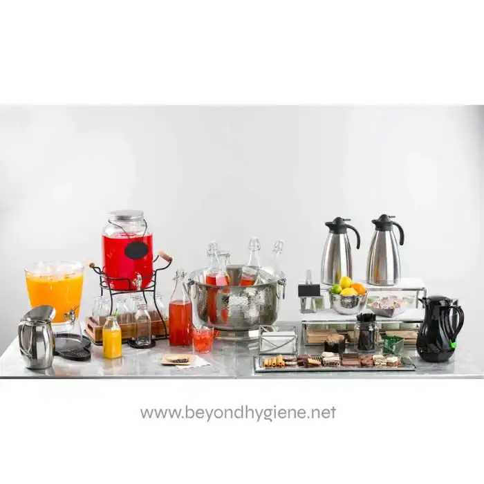 Juice dispenser with beverages and glassware at a catering station, beverage service setup, Beyond Hygiene Asia, event catering, hygienic beverage service, professional food and drink hygiene solutions.