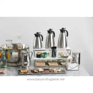 Coffee station setup with stainless steel hot water dispensers and assorted beverages, snacks, and cups for a hospitality or corporate environment - Beyond Hygiene Asia.