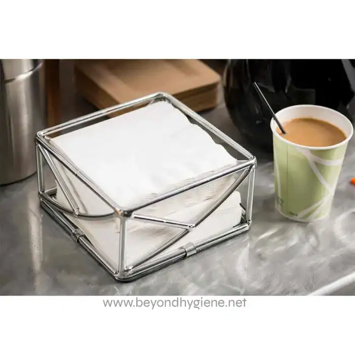Paper towel holder with white paper towels on a stainless steel countertop in a professional cleaning or hygiene setting.