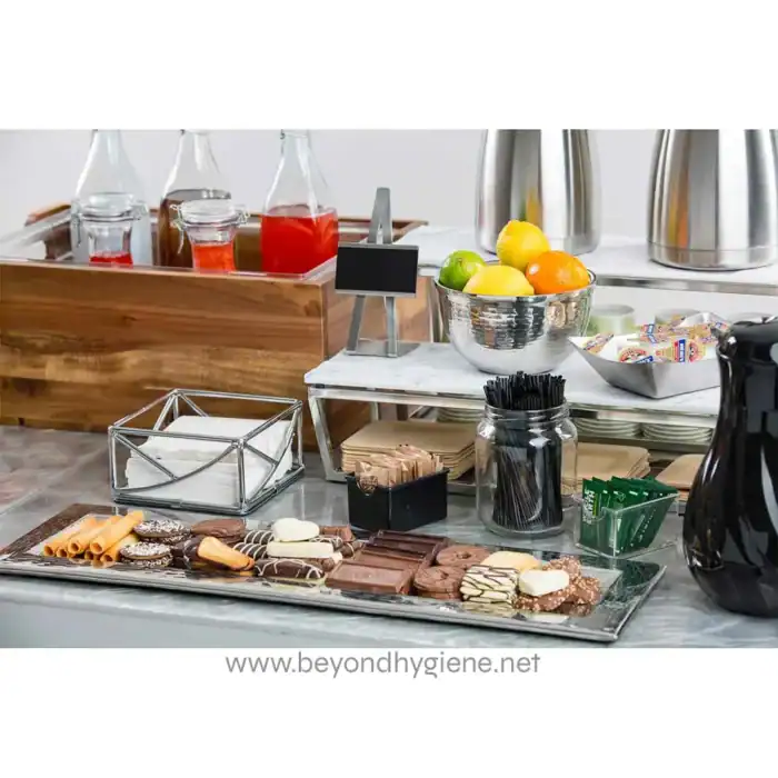 Assorted desserts and snacks on a coffee table in a modern hotel or cafe setting, with fresh fruits and beverage station, showcasing hygiene and cleanliness in food presentation.