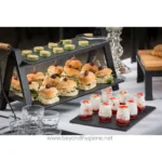 Mini sandwiches, salads, and desserts displayed on black serving trays at a catering event, emphasizing hygiene and food presentation for corporate or event catering.