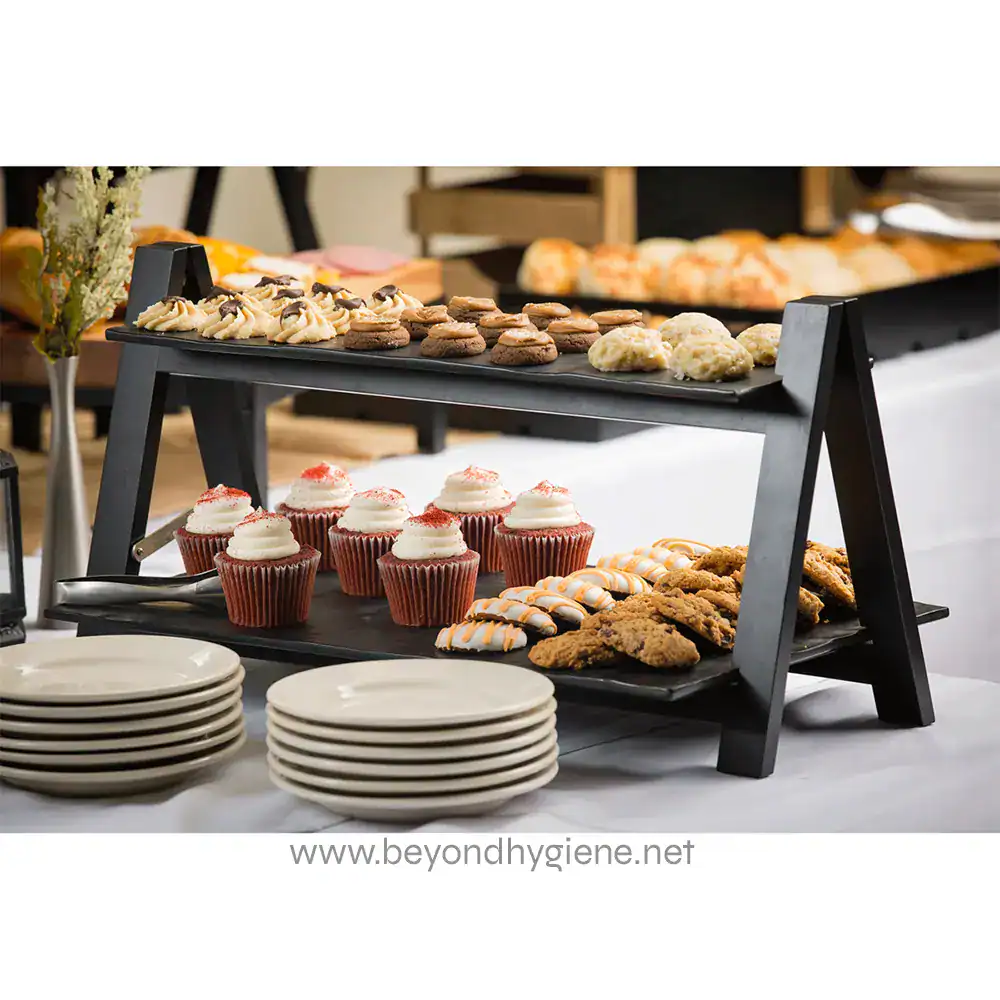 MG1_ENV-06 Freshly baked cupcakes, cookies, and pastries displayed on a black two-tier food stand at a catering event, emphasizing food safety and hygiene.