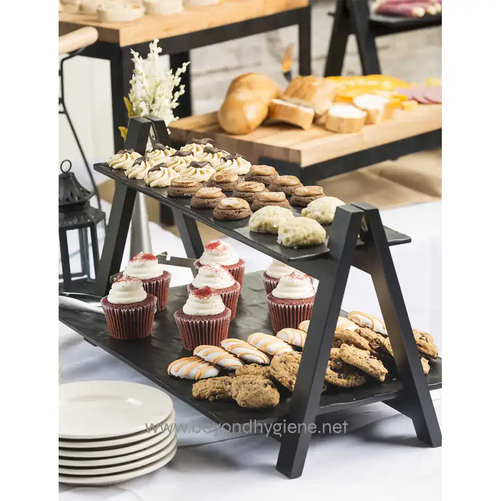 MGL2_ENV_2 Delicious assorted desserts and baked goods on a black multi-tiered serving stand at a catering event, showcasing professional hygiene standards in food presentation and safety.
